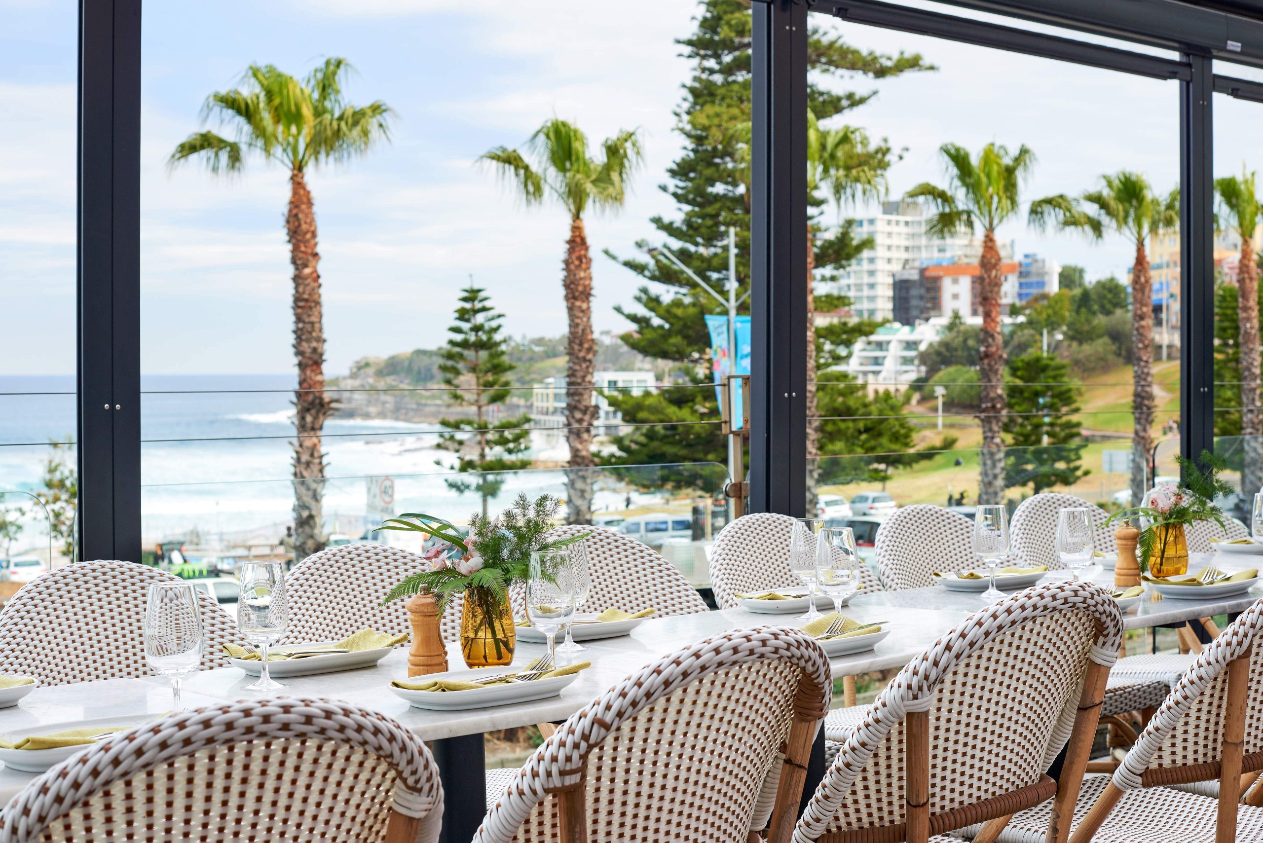 An outdoor restaurant with views over the beach, with palm trees and the sea in the background