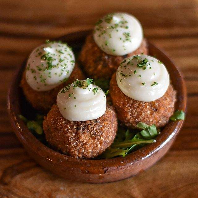 A dish of four little fried balls with aioli sauce on top and herbs in a small brown plate at a restaurant