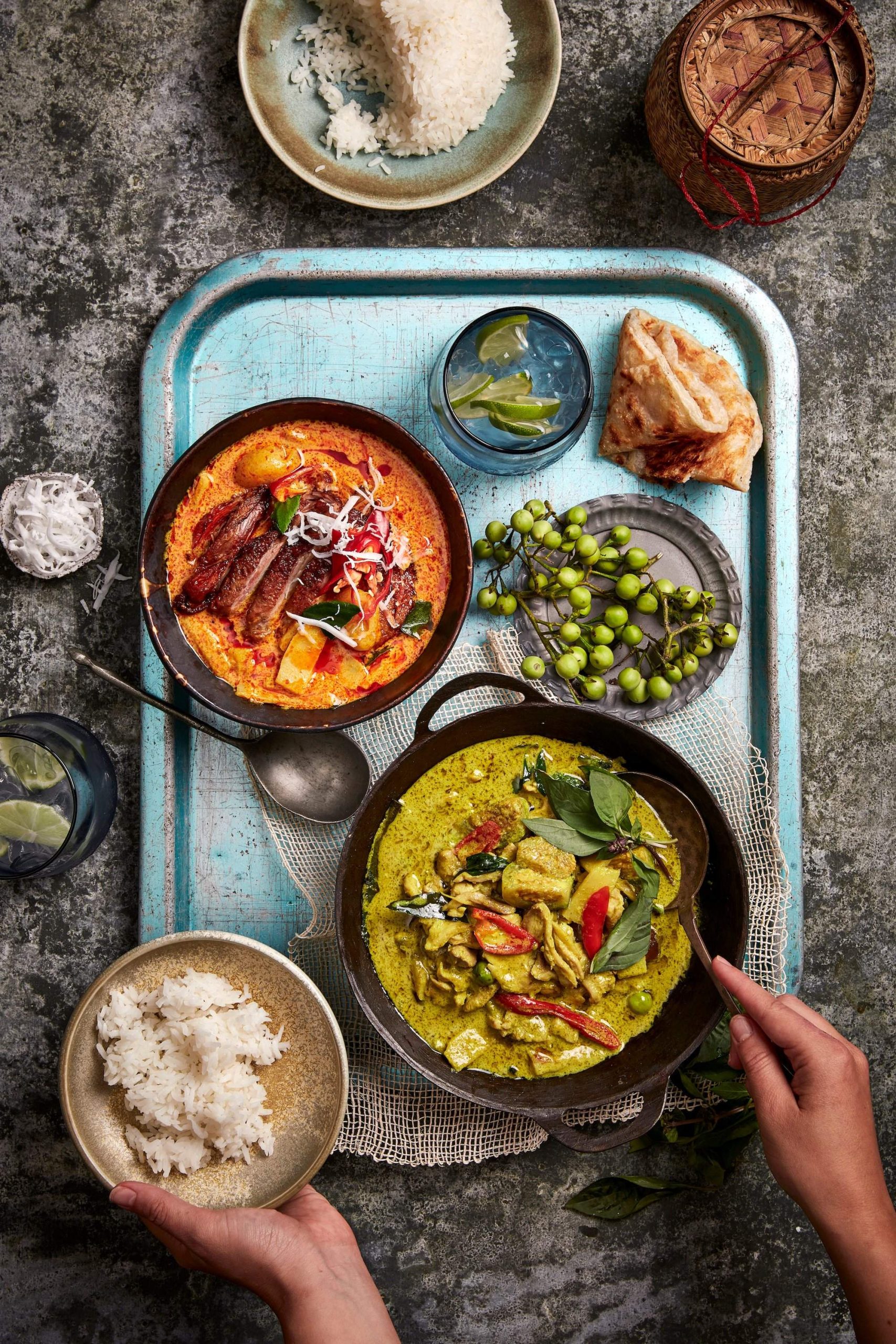 A bowl of green curry and a bowl of red curry with two bowls of rice at Khao Pla, a restaurant in Sydney