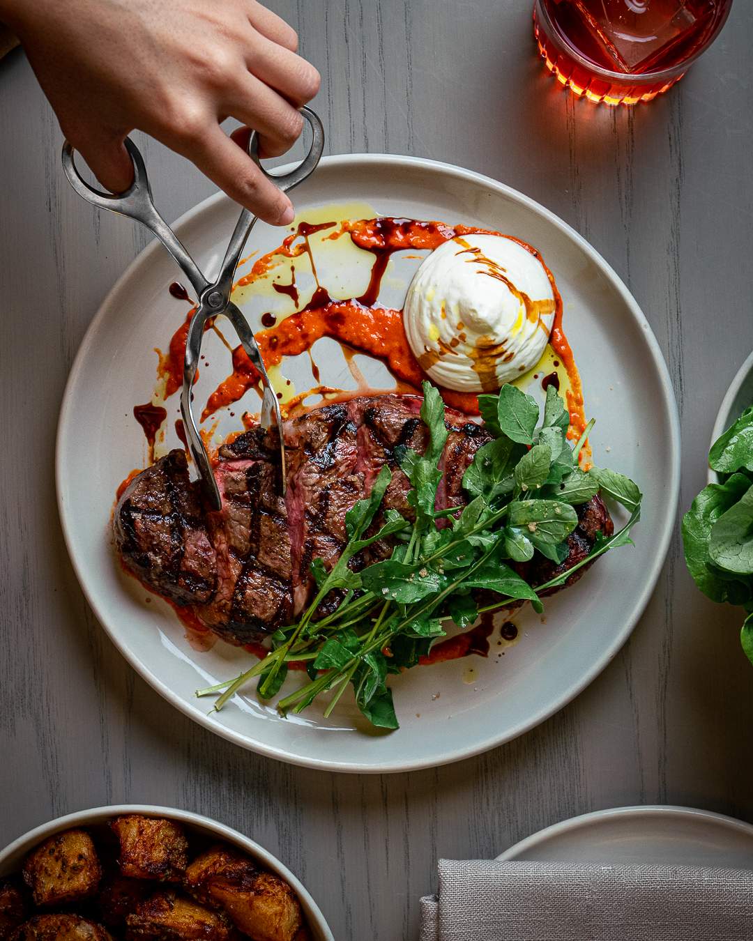 A white plate with a steak, salad leaves, a white sauce and red jus on a restaurant table.