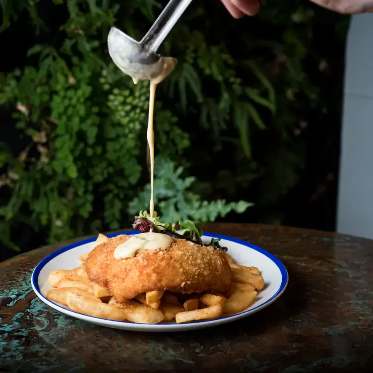 Someone pours cheese sauce over a chicken schnitzel and fries at The Bar at The Rose of Australia Hotel