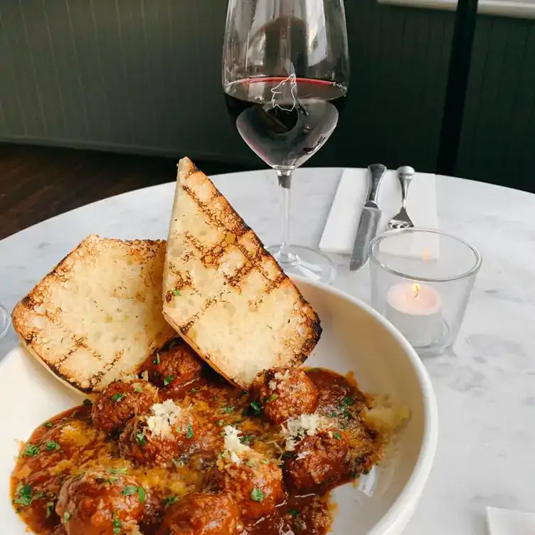 A white bowl with meatballs in tomato sauce and two toasts and a glass of red wine at The Wolf Windsor in Melbourne