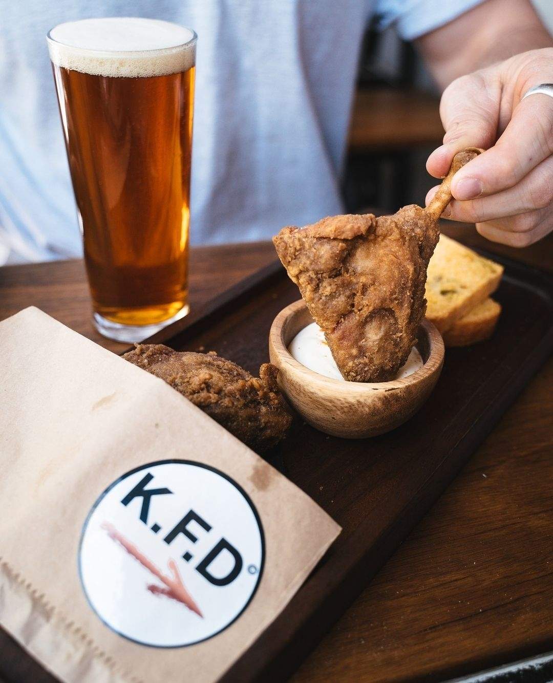 Korean fried duck being dipped into sour cream next to a schooner of beer