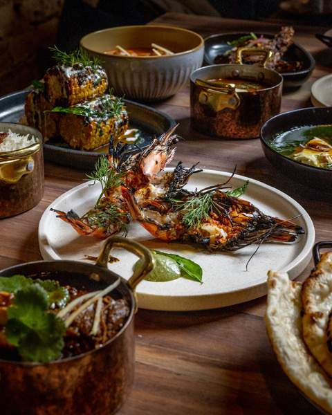 A table with various small dishes, including prawns, corn and curries.