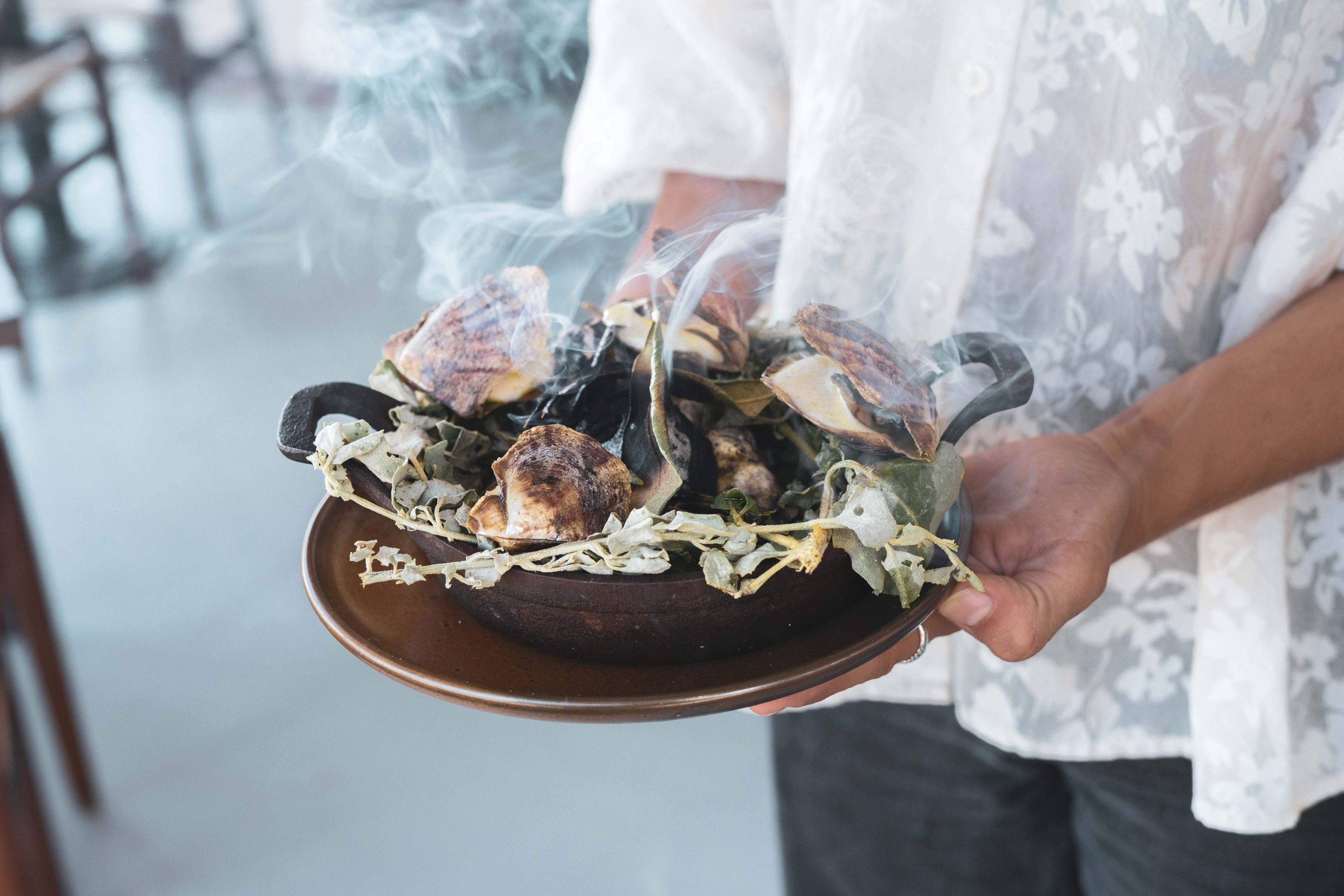 A woman holding a brown plate with Akoya oysters on hot coals