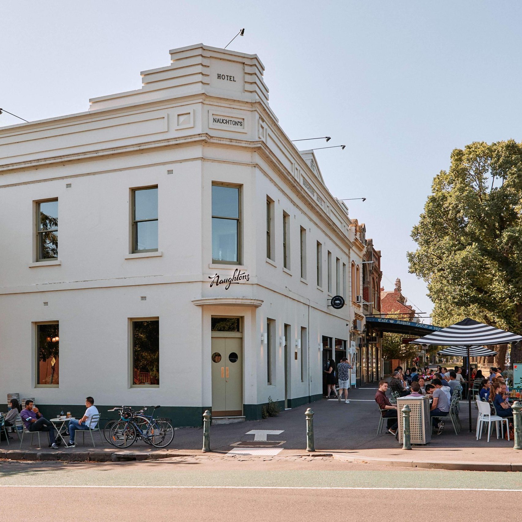 The facade of an old white building, with a sign that says Hotel Naughton's, with an outdoor seating area during daytime