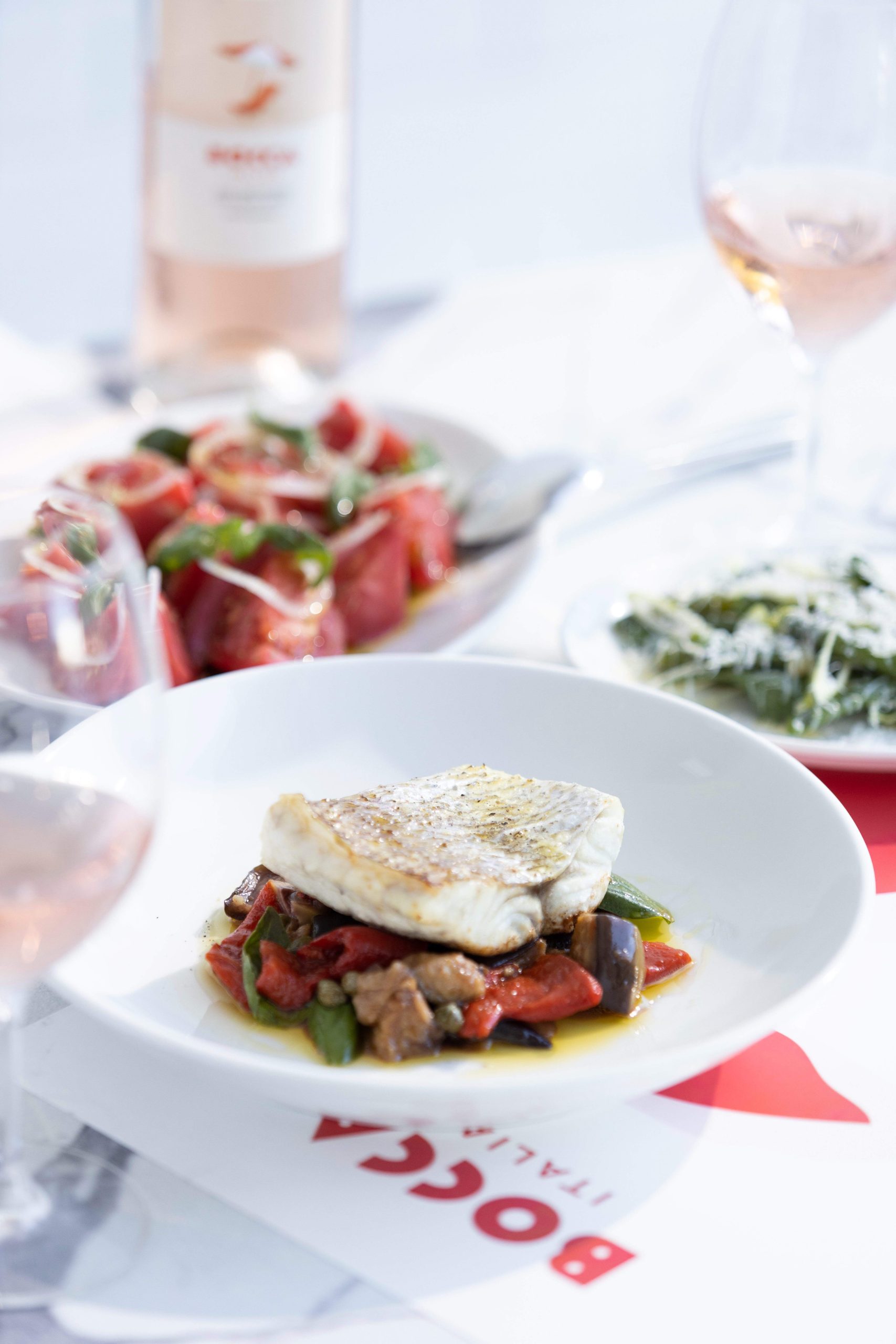 A dinner table set with rose, a white bowl with market fish, and side salads