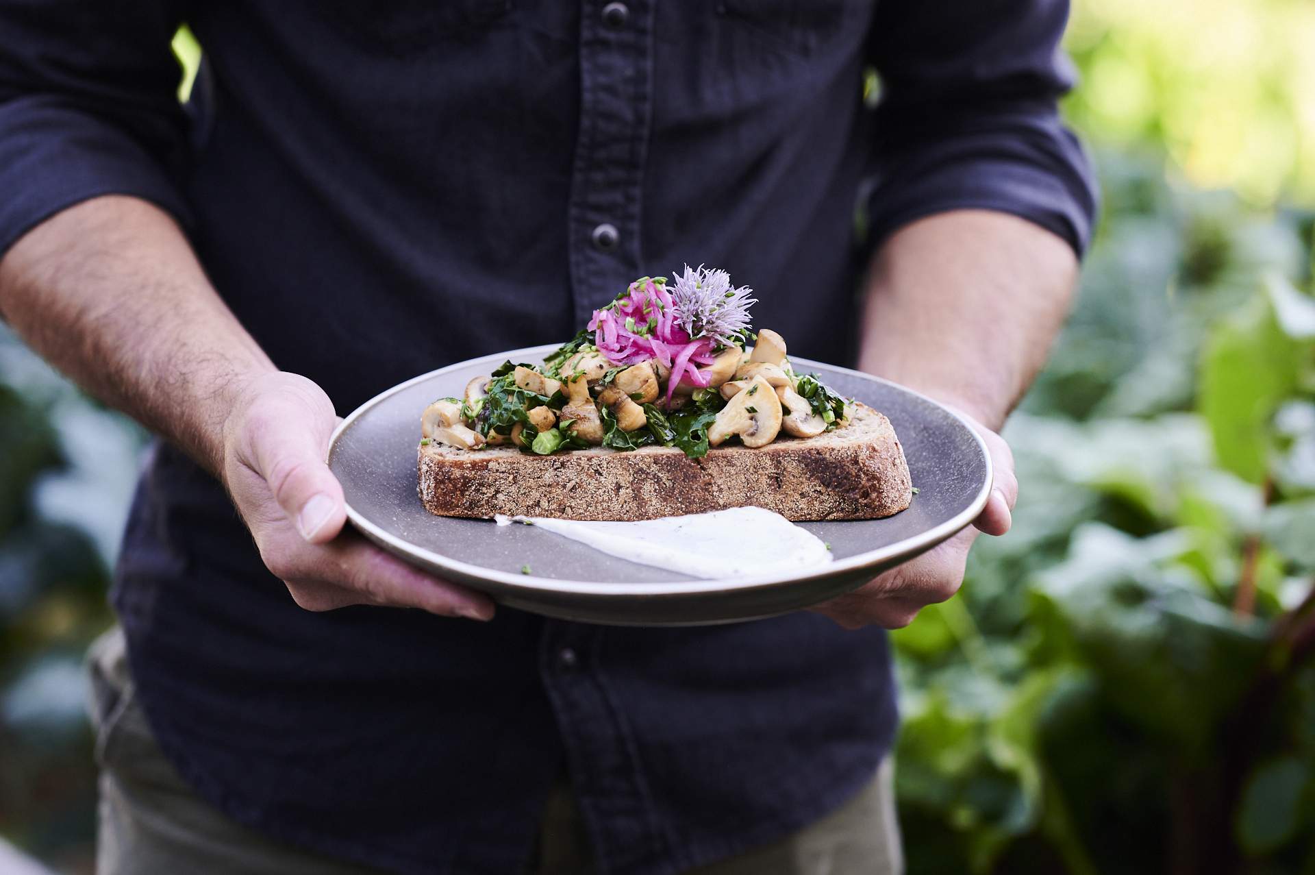 A man holding a plate which has a piece of toast with mushrooms on it at Canberra cafe Two Before Ten.