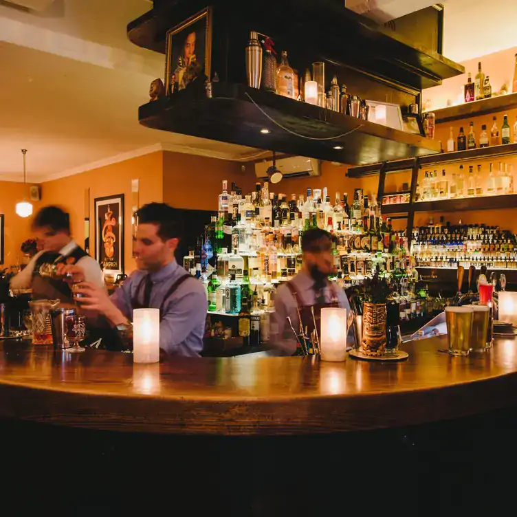 Bartenders and mixologists prepare cocktails behind a dimly-lit bar with bottles lined up on shelves at Lily Blacks