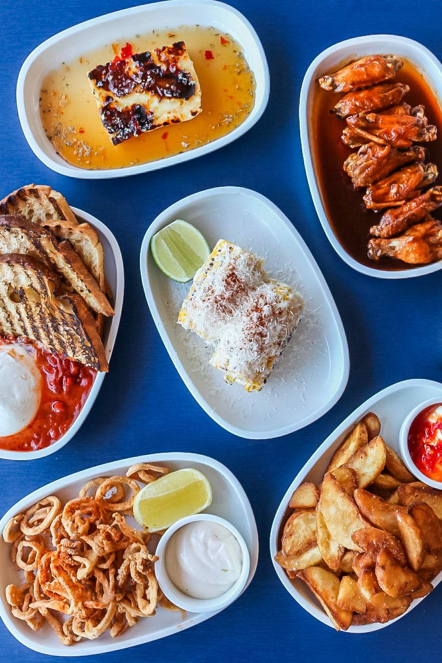 A blue table showcases an array of dishes and small plates, including fries, chicken wings, toasted bread and fried calamari at Curly Lewis Brewing Co., a restaurant in Sydney.