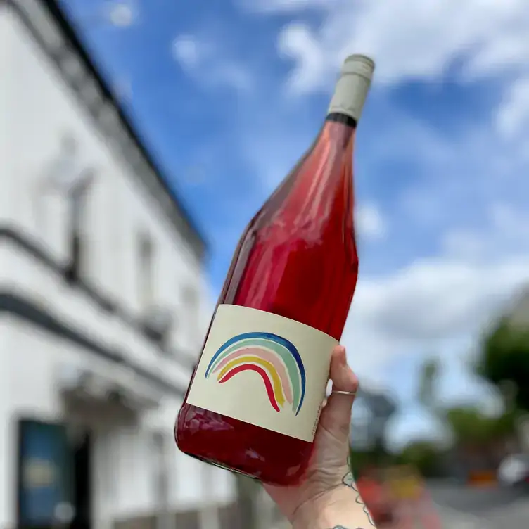 A diner holds a bottle of rosé wine featuring a label with a rainbow at Marquis of Lorne