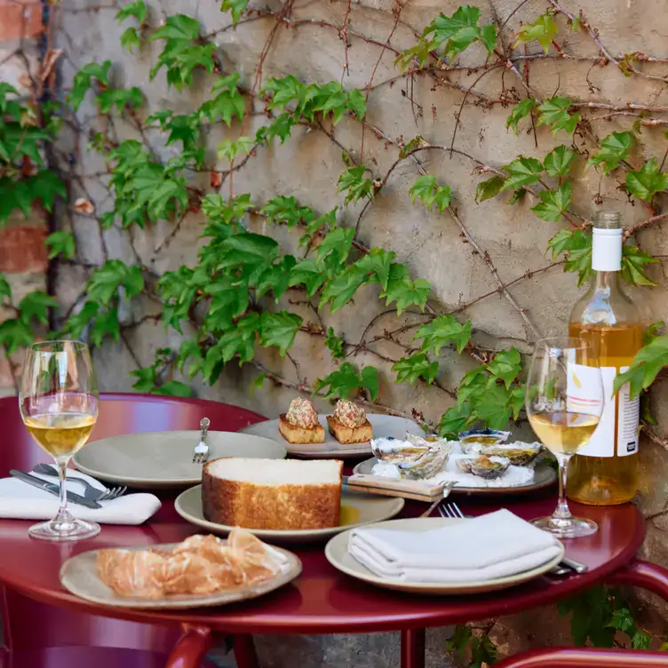 An outdoor dining set up with small plates and white wine and a leafy ivy in the background at Clover