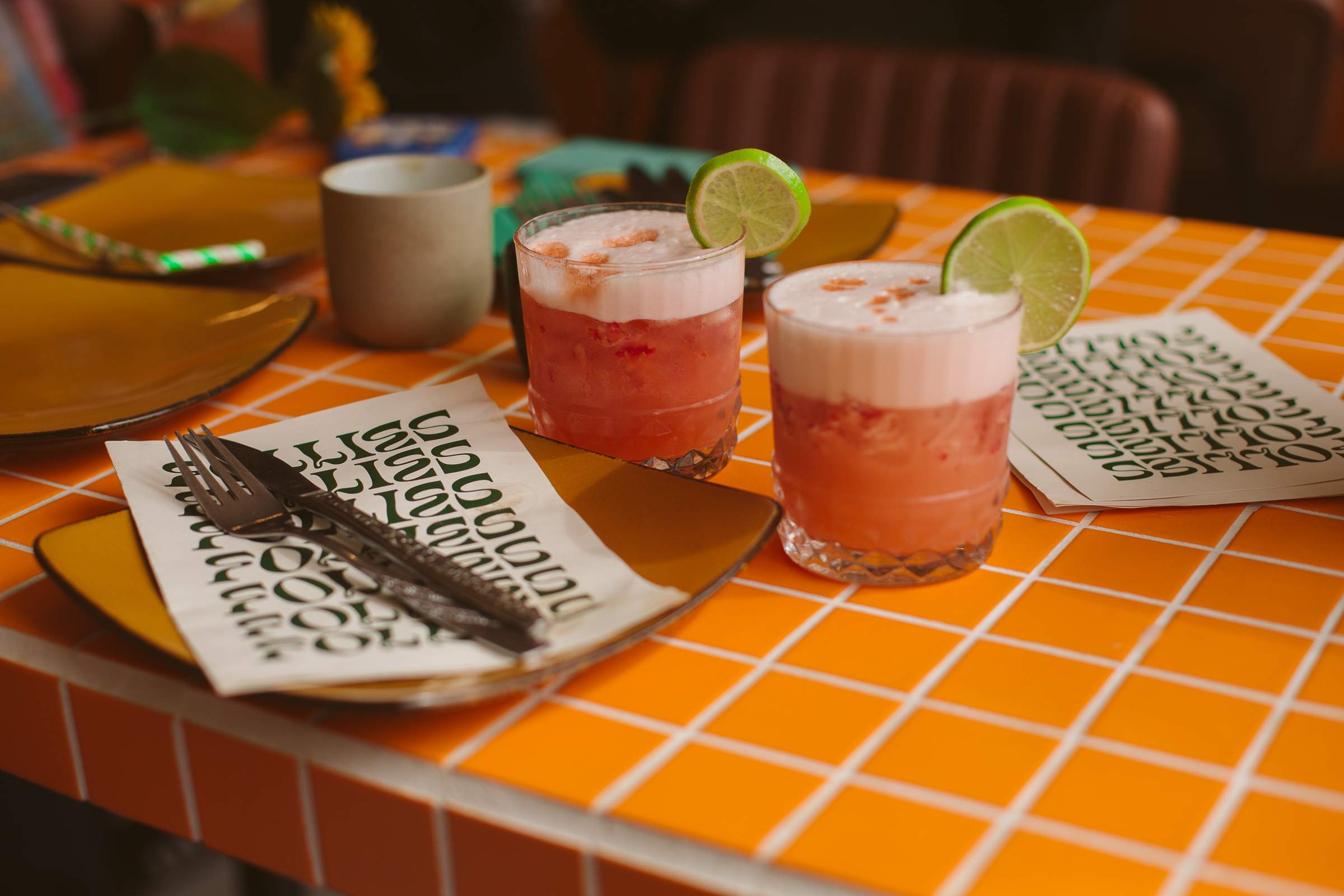 Two bright orange cocktails with foam tops sit atop a bright orange table with menus at Follies Bar in Melbourne