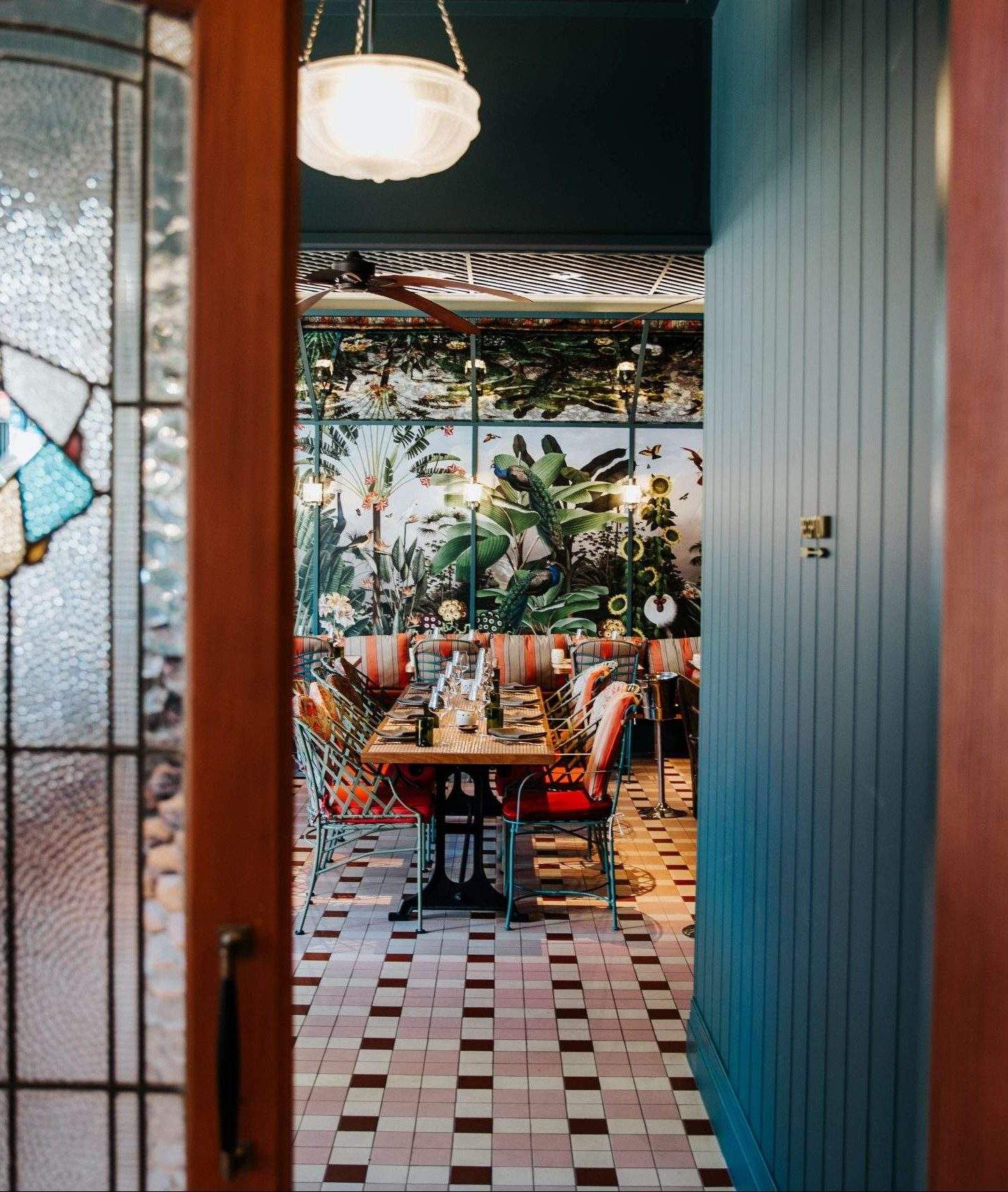 The interior of Ovolo Group Brisbane restaurant ZA ZA TA featuring stained glass doors, blue paneled walls, and striped orange and grey chairs.