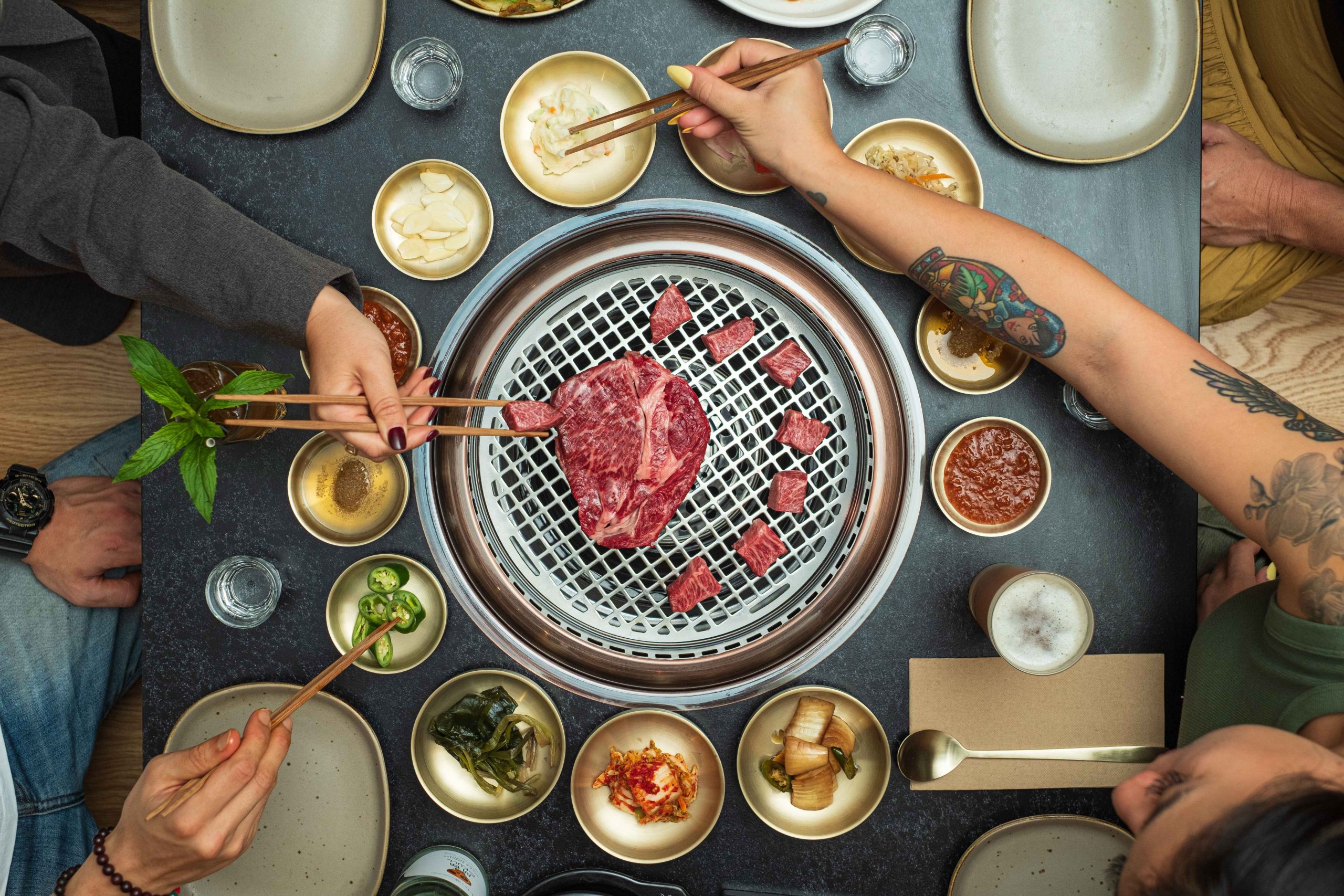 Diners cooking wagyu on Korean barbecue grill with a selection of side dishes at Soot in Sydney