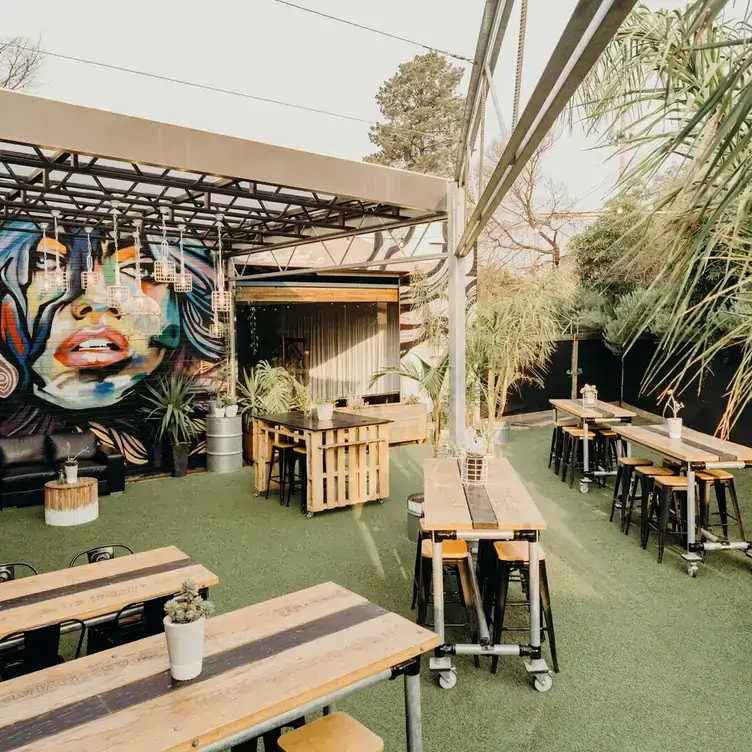 An outdoor dining space featuring wooden tables and benches, and wall art at The Budgie Bar in Melbourne.