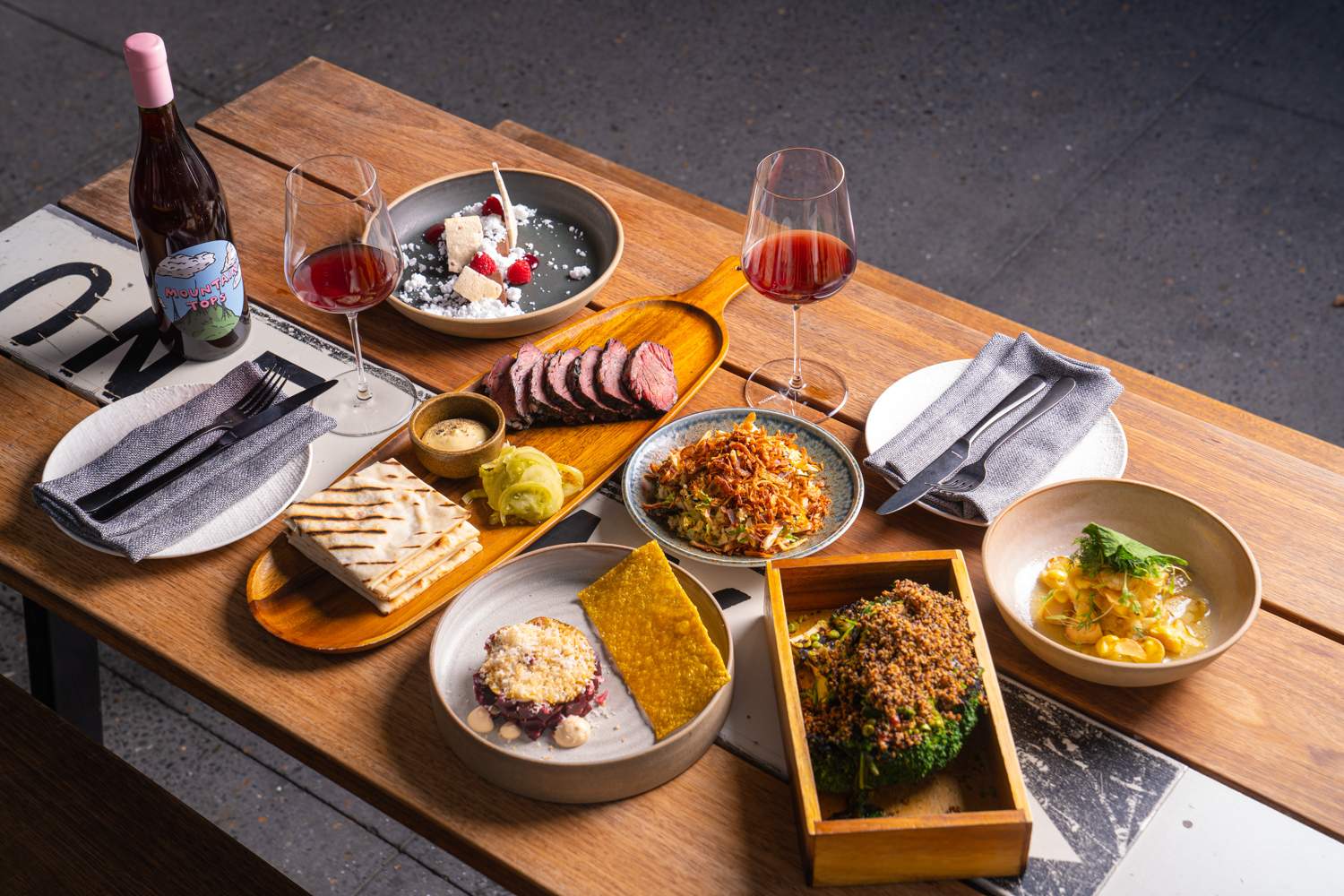 A wooden table covered with a variety of shared plates and two glasses of natural wine at Detour in Woolloongabba