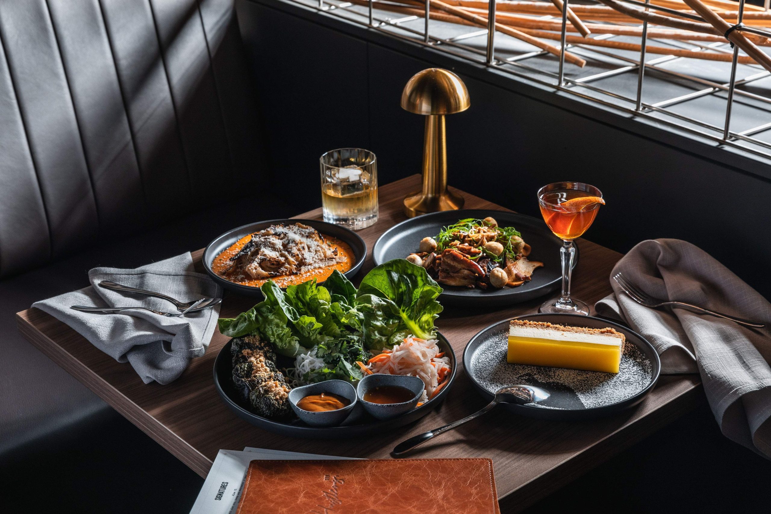 Three dishes, two drinks, and one menu placed on a wooden table at Sydney restaurant Hustlers.