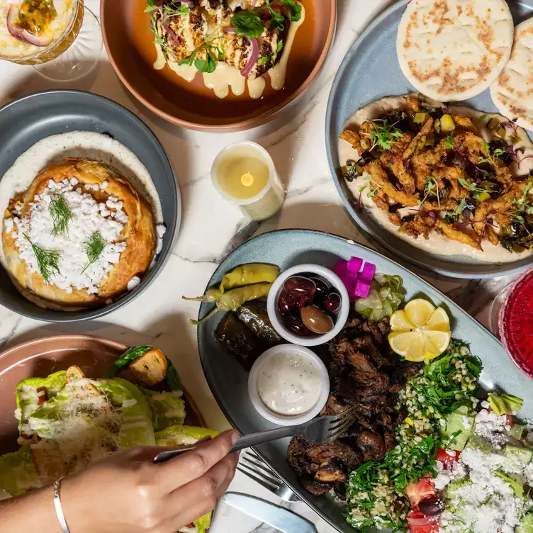 Someone reaches with a fork across a table laid with multiple dishes including salads at Mina Maria, one of the best vegan restaurants in Sydney.