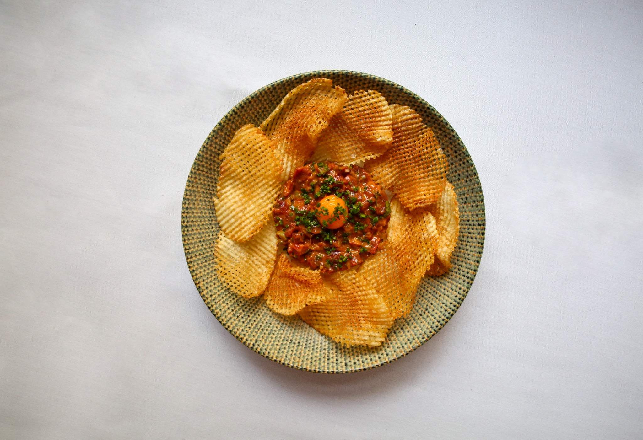 Beef tartare topped with egg yolk and parsley and surrounded by thatched potato crisps in a ceramic bowl at French Saloon restaurant in Melbourne.