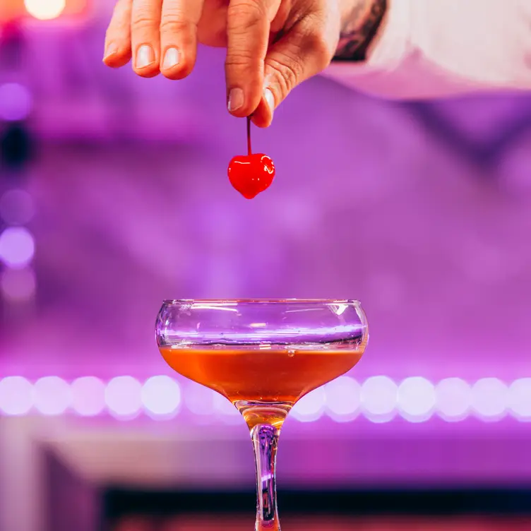 A hand holds a cherry on top of a red-colored cocktail at Good Love in Melbourne