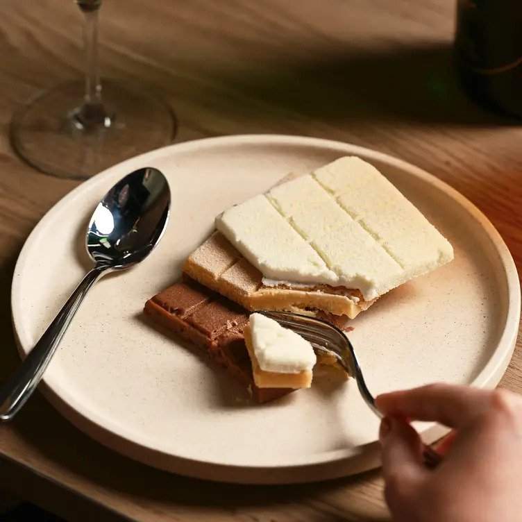 A hand holding a fork samples a salted cashew praline, banana, and coconut dessert at North & Common restaurant in Melbourne.