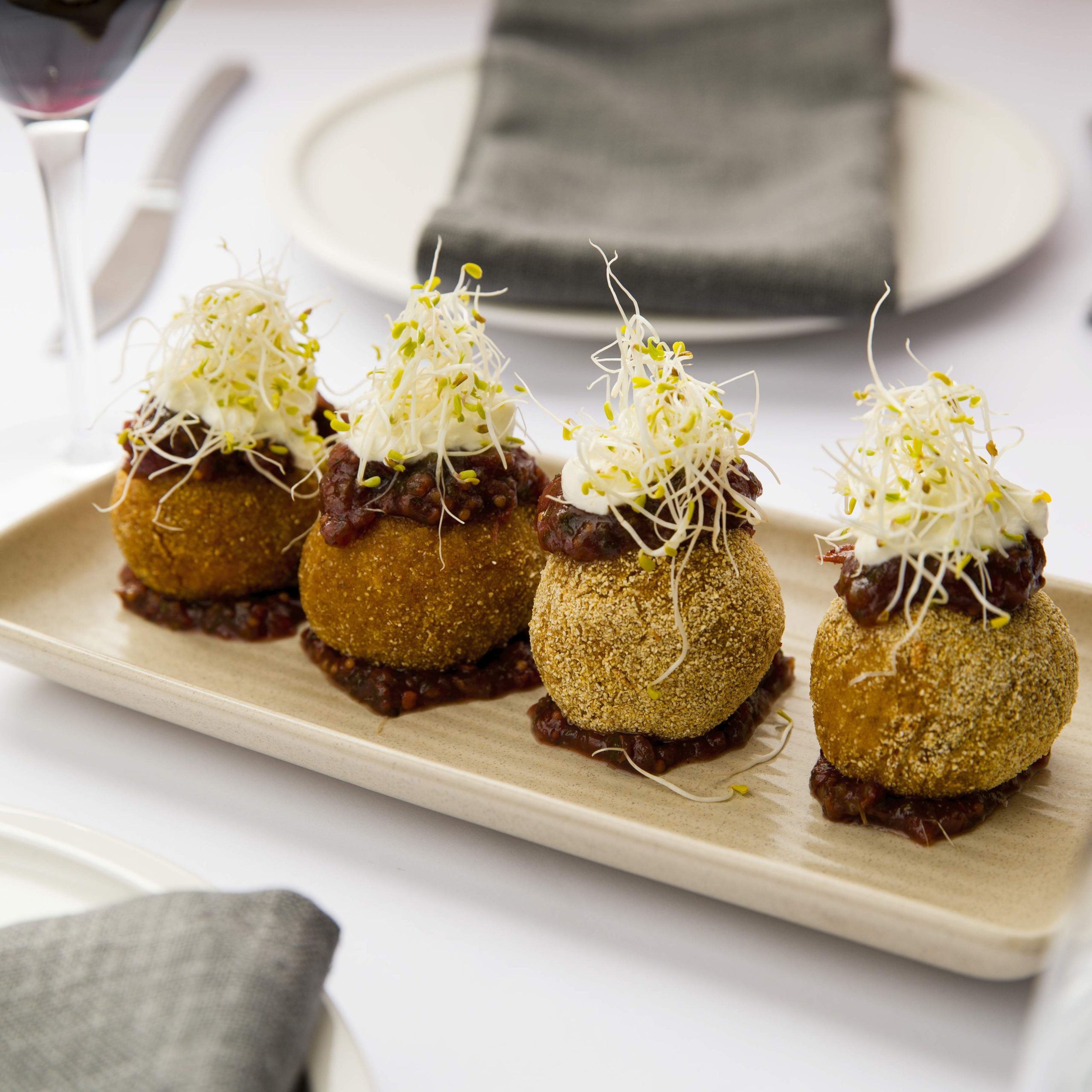 Four arancini balls lined up on a white plate topped with chutney and herbs at Rubyos in Newtown.