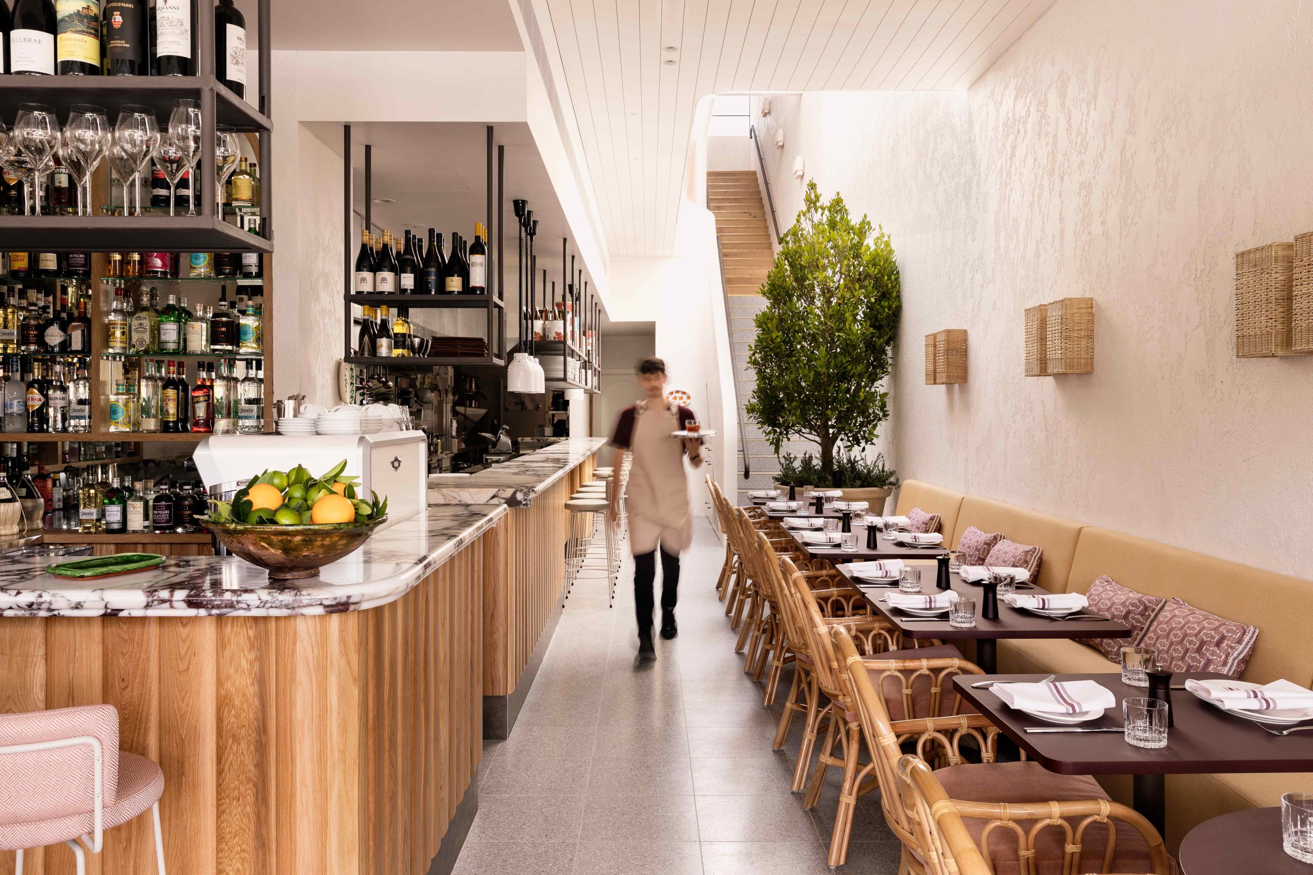 A waiter walks through Grazia Restaurant in Melbourne with a well-stocked marble bar and booth seating in the foreground.