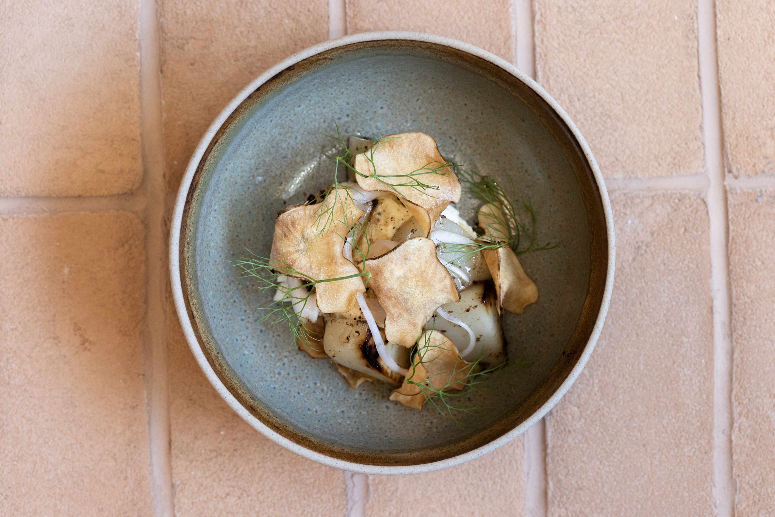 A ceramic bowl holds jerusalem artichoke, stracciatella, and black truffle atop terracotta tiles at Enoteca Boccaccio in Melbourne.