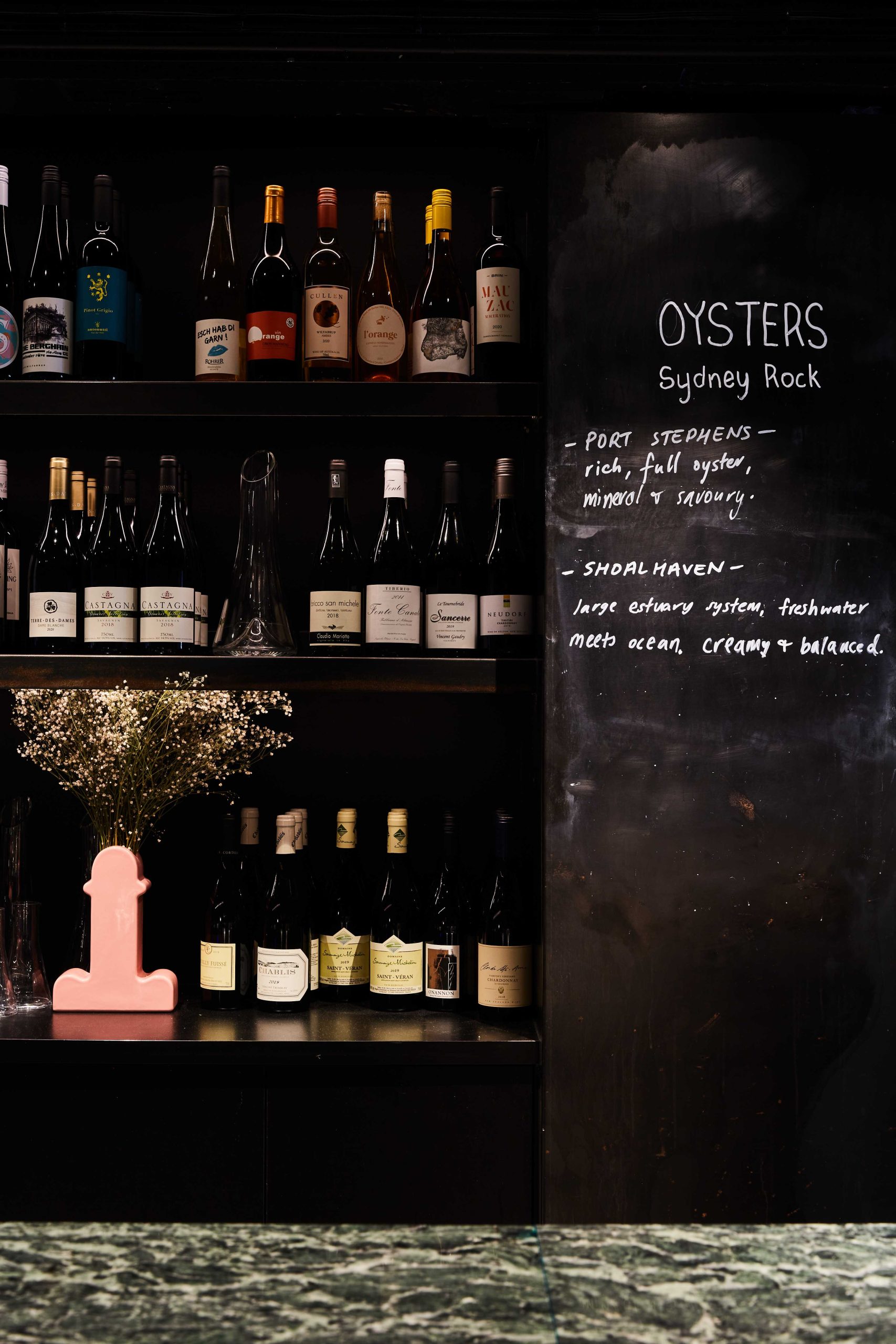 Wine bottles on shelves next to a chalkboard displaying an oyster selection at Essa in Brisbane, one of the best restaurants in Australia