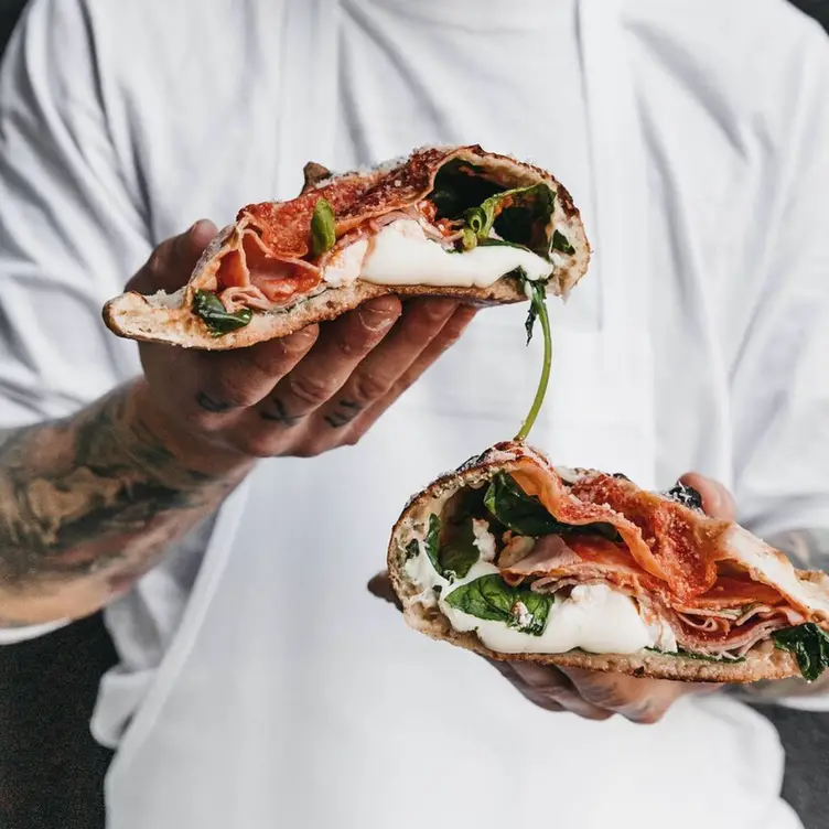 Someone holds up a calzone, cut in half to reveal the filling at DOC Pizza, one of the best Italian restaurants in Melbourne.