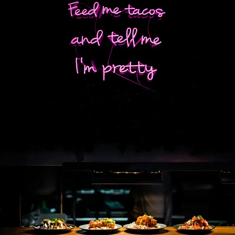 Four dishes from Hail Mary lined up under a neon-lit sign reading ‘Feed me tacos and tell me I’m pretty’ at Hail Mary, one of the best vegan restaurants on the Gold Coast.