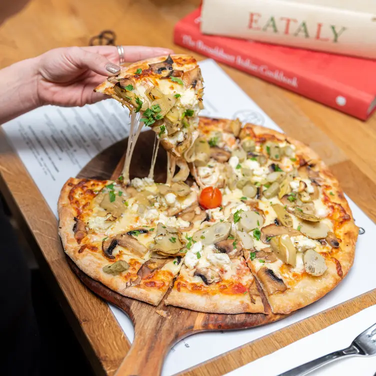 A hand taking a slice of pizza from a large pie at Maccaroni Trattoria Italiana – one of the best Melbourne vegetarian restaurants.