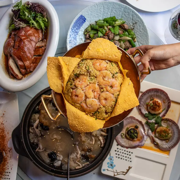 A dish being passed over other dishes on the table of Secret Kitchen – Chinatown, one of the best Chinese restaurants in Melbourne.