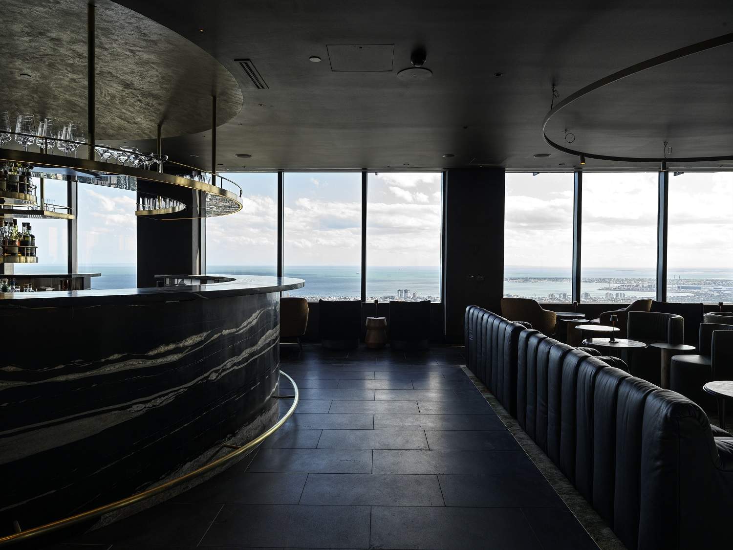 Dark granite bar and tiles with hints of natural brass in the forefront and sweeping views over the bay in the background at Lui Bar in Melbourne.