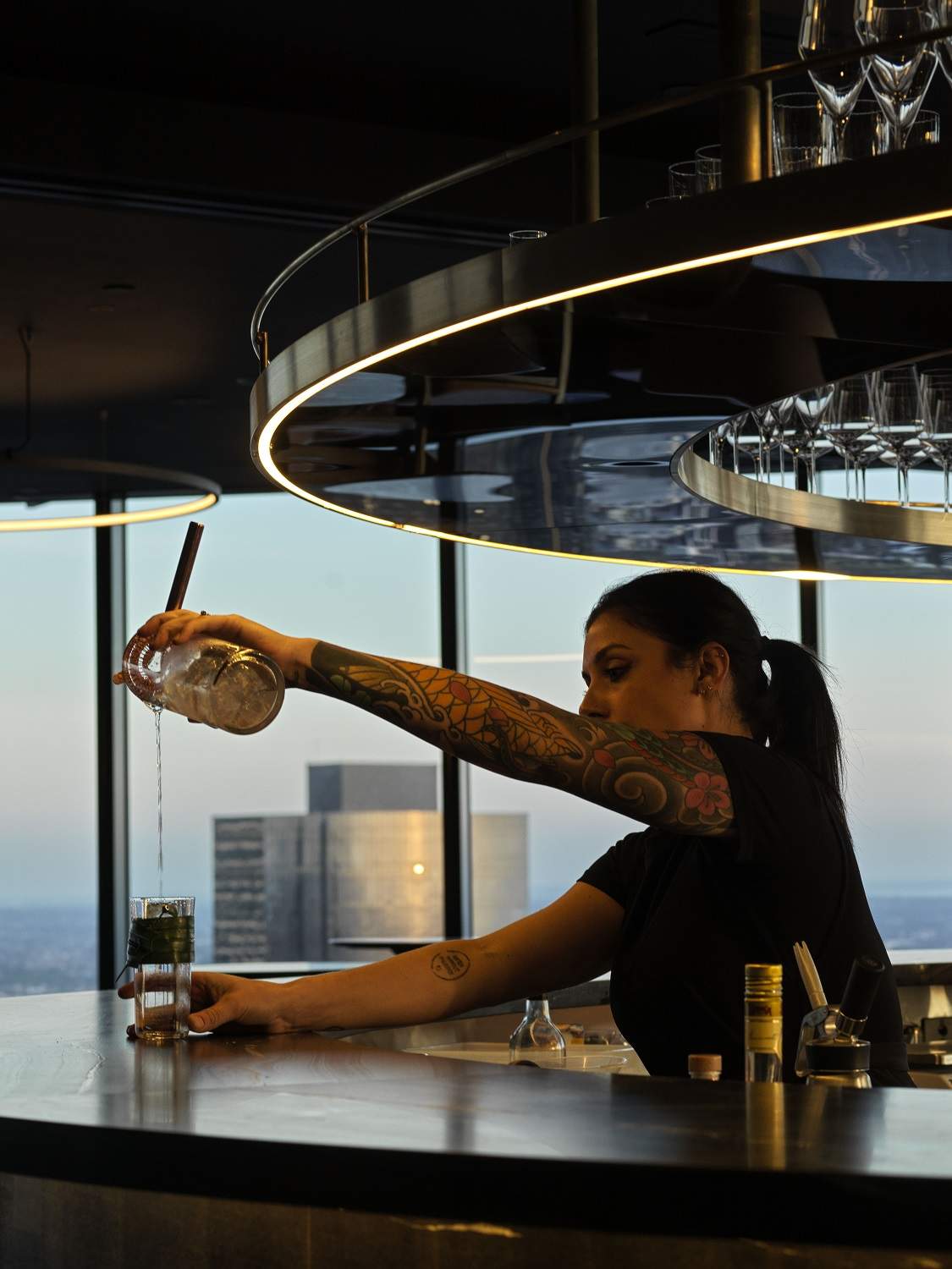 A mixologist pours out a cocktail from a shaker into a highball glass on the granite bar top of Lui Bar in Melbourne.