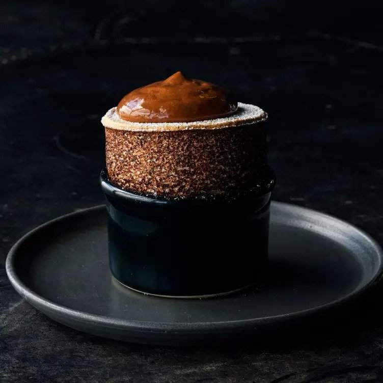 A chocolate soufflé rises out of a dark ceramic ramekin atop a black marble table at the restaurant Vue de monde in Melbourne.