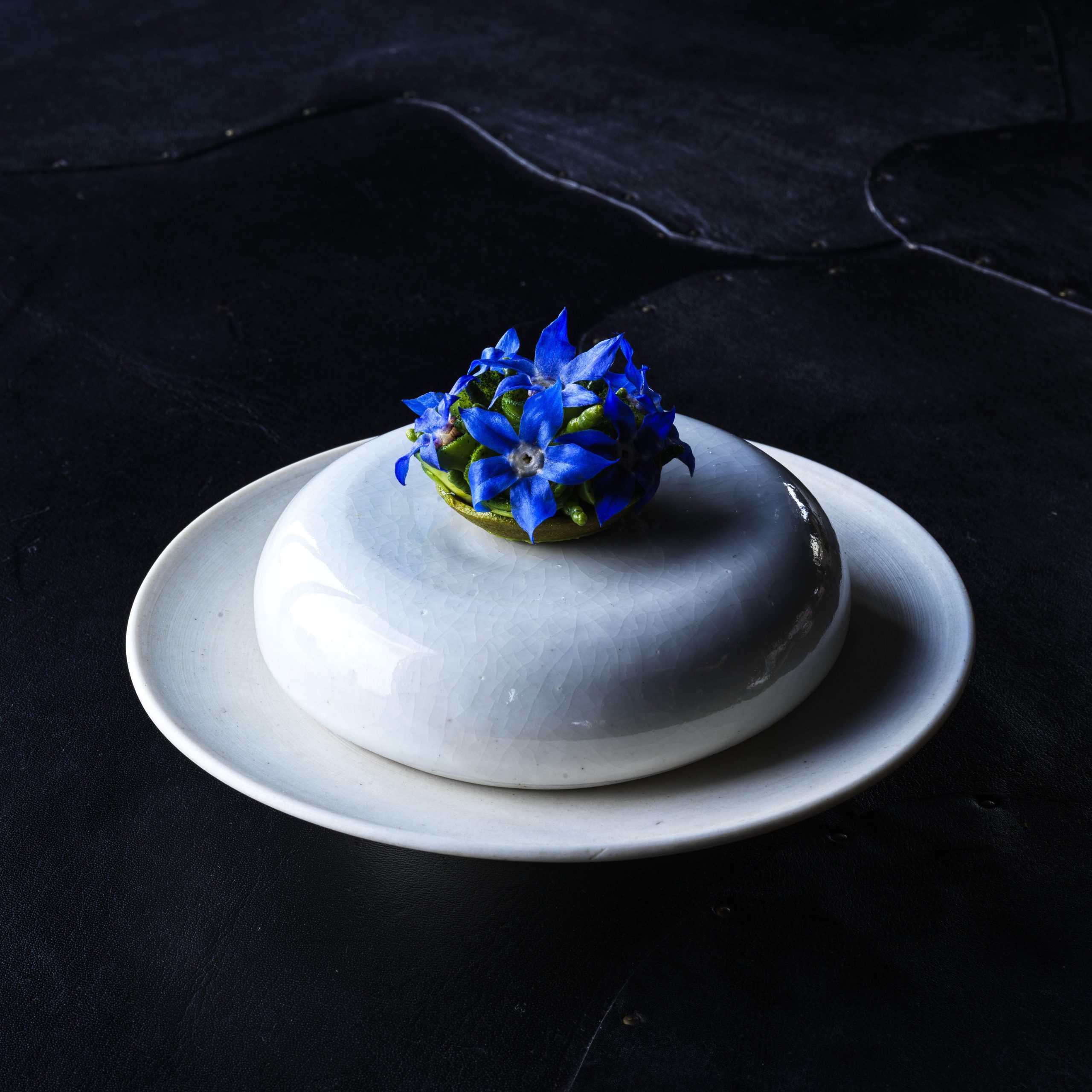 A tart of avocado puree, avocado leaf oil, and finger lime finished with herb emulsion and borage flowers sitting atop a white ceramic plate at Vue de monde in Melbourne.