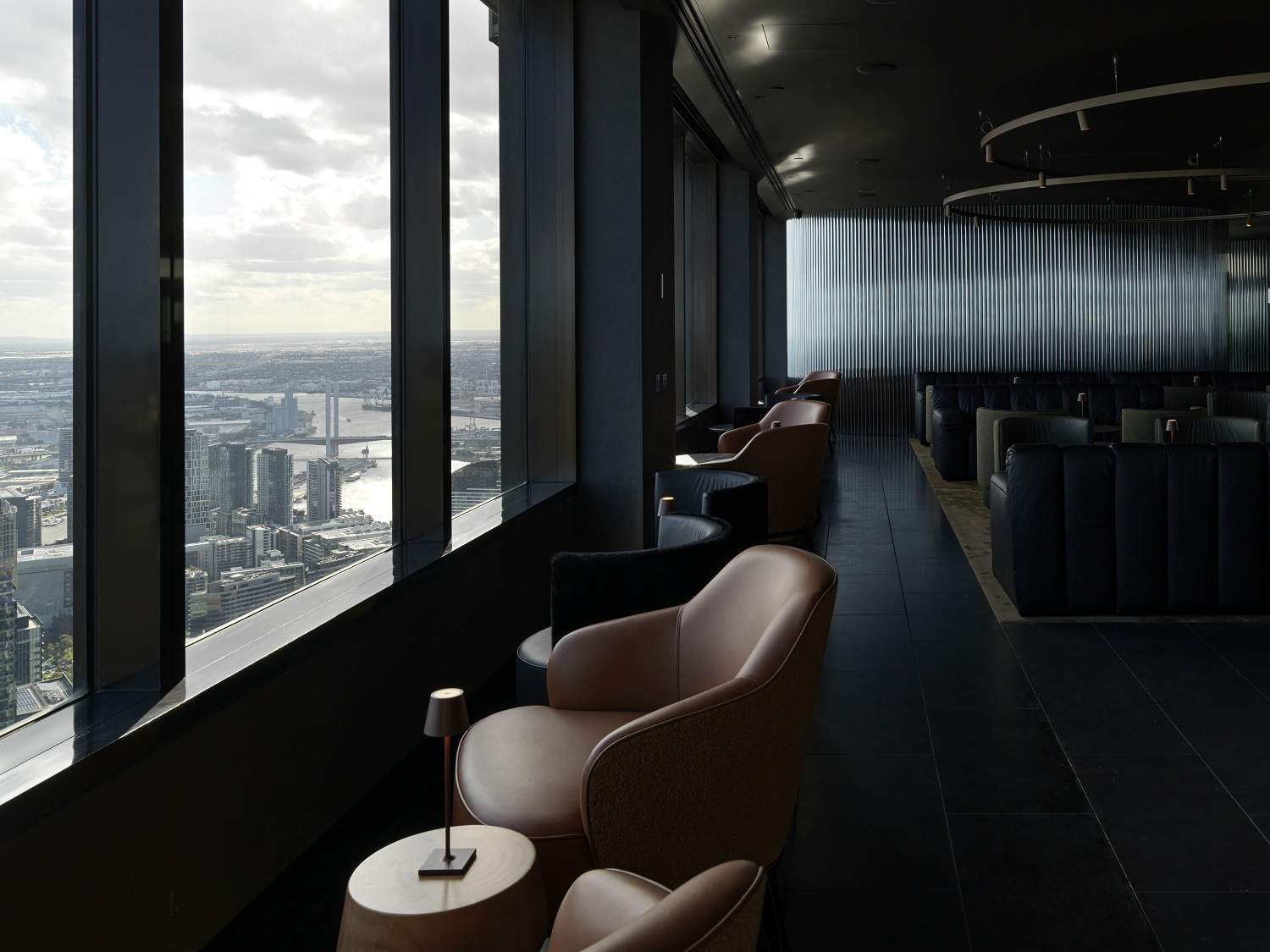 Earthy toned leather booths and chairs standout from the dark, muted tones of Lui Bar that shows views across Melbourne.