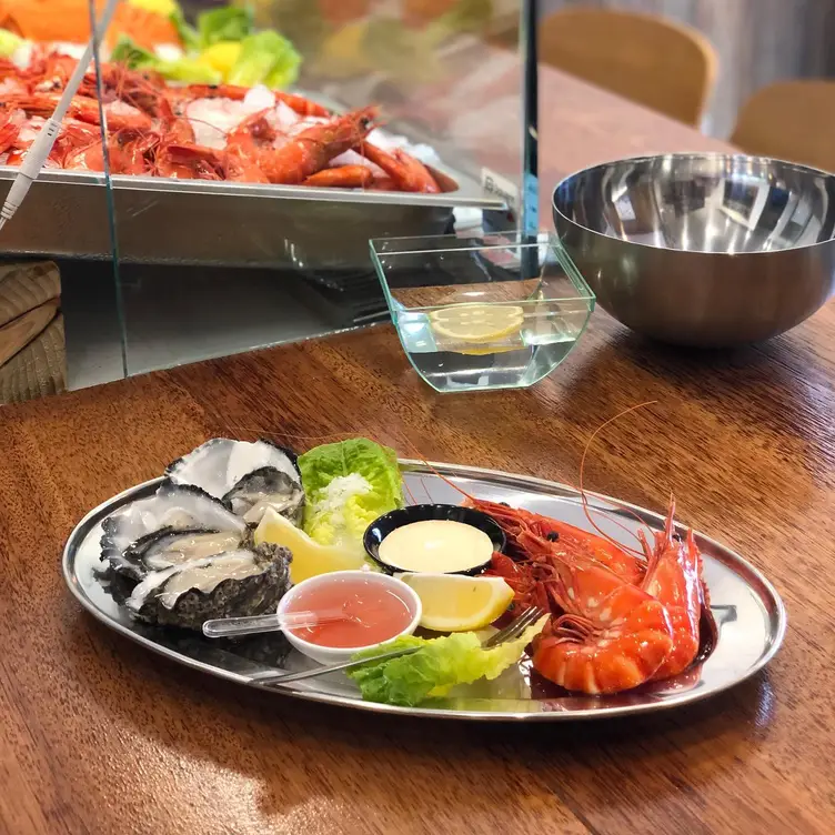 A plate with oysters, prawns, dipping sauces and lemon wedges, served at BLU OYSTER CO., one of the best seafood restaurants in Melbourne.