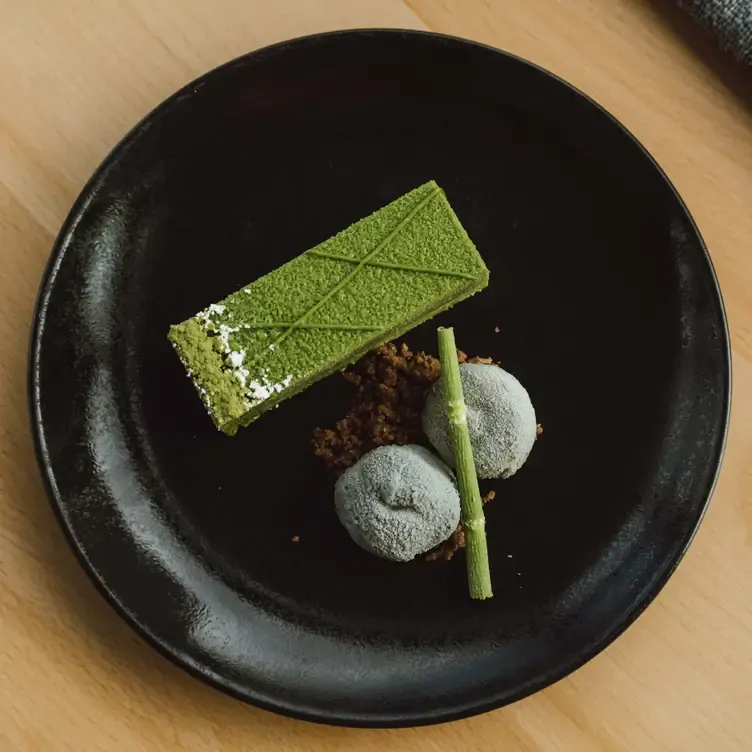 A dessert at Koomo Restaurant and Bar, made up of a green slice, brown crumble and grey biscuits to create an earthy look.