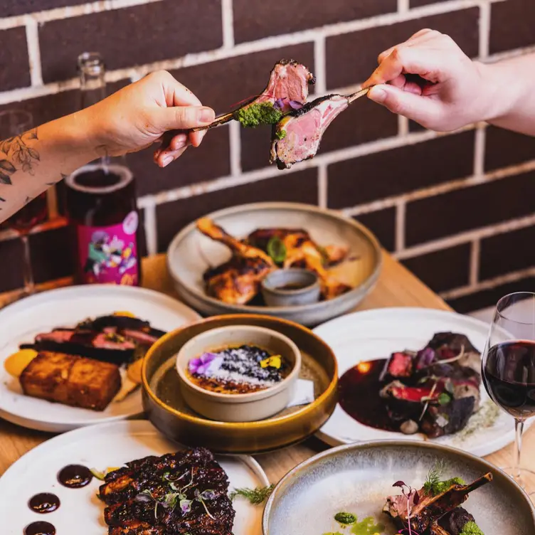 Two diners ‘cheers’ a dish of meat on the bone at Auvers Dining Rhodes, one of the best French restaurants in Sydney.