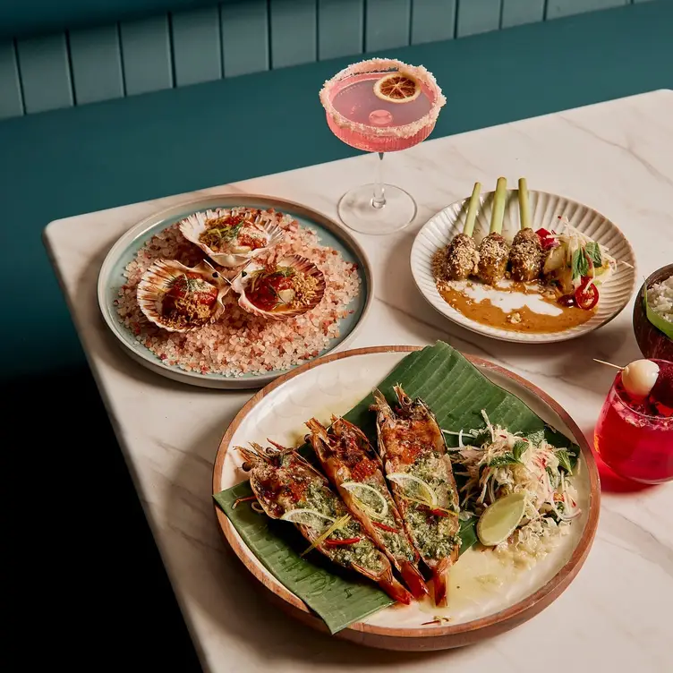 A table with a few seafood and vegetable dishes served alongside cocktails at Kan Eang by Thai Culinary, one of the best Thai restaurants in Melbourne.