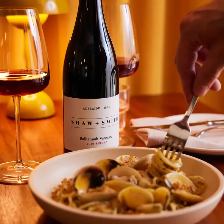 A diner twirls some seafood pasta around their fork with a glass and bottle of wine on the table at Longplay Bistro, one of the best date night restaurants in Adelaide.