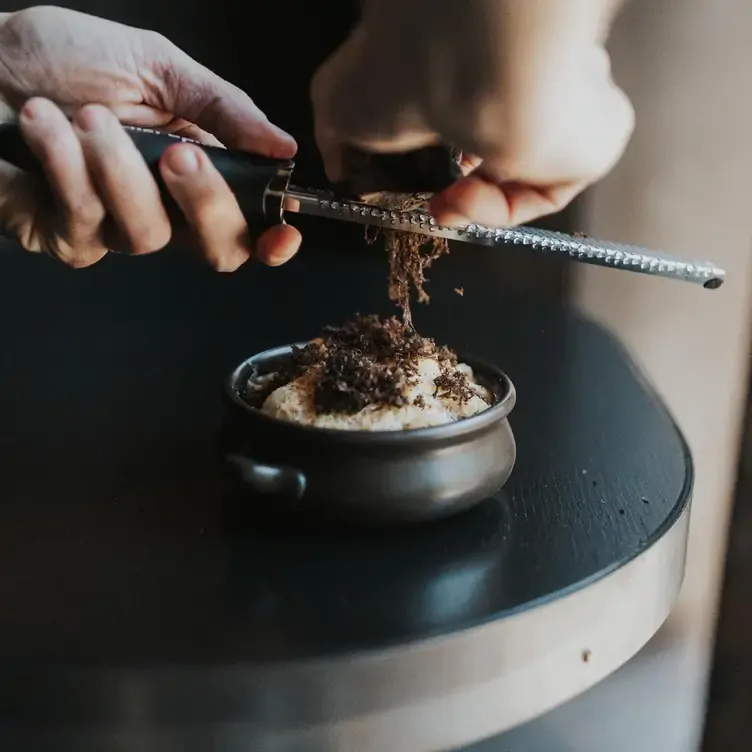 A chef grating the topping onto an entree at Essa Restaurant, one of the best date night restaurants in Brisbane’s Fortitude Valley.