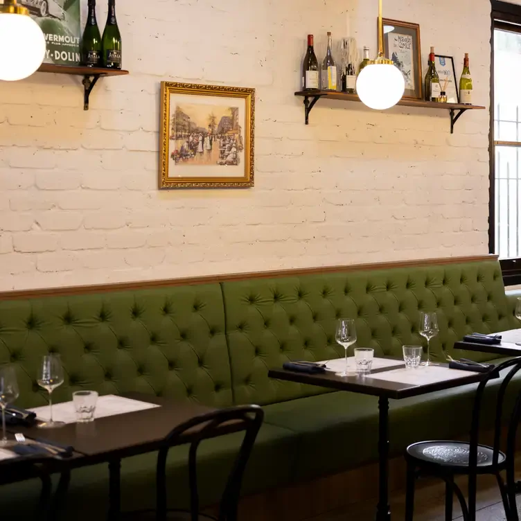 The interior of Bistro Francais, one of the best romantic restaurants in Adelaide, with plush, green seating, framed art and shelves of wine.