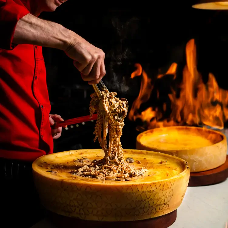 A chef twirls some pasta over a wheel of cheese at Godi La Vita, one of the best date night restaurants in Adelaide.