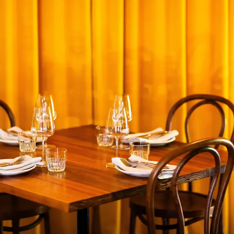 A table at Longplay Bistro set with plates, cutlery and glasses. A warm yellow curtain hangs in the background.