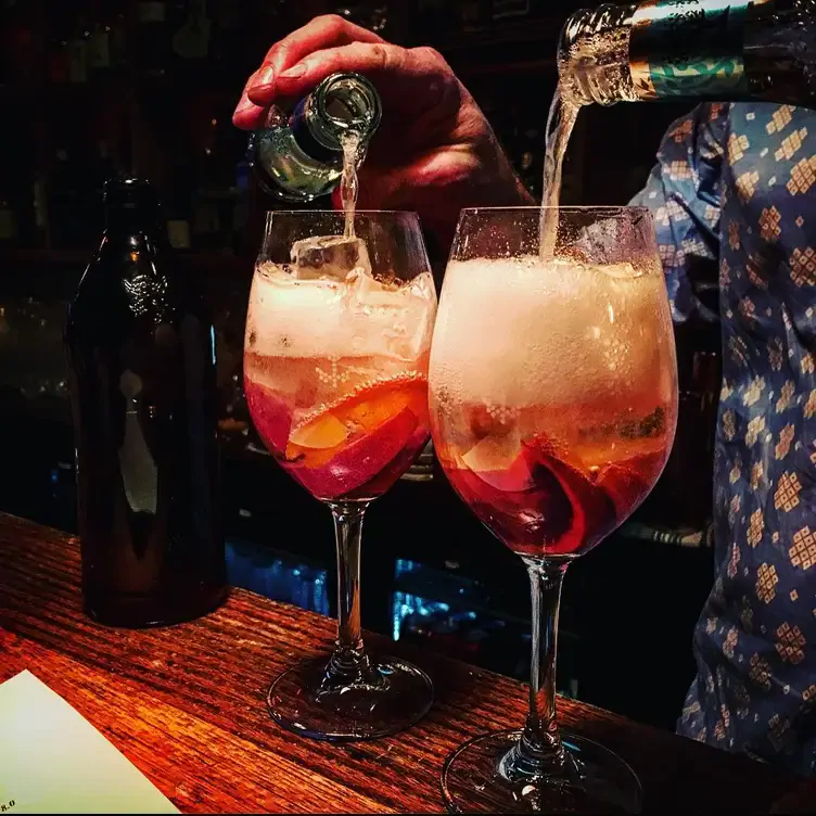 A staff member at Udaberri Pintxos Y Vino tops up two glasses filled with liquid and fruit peel.