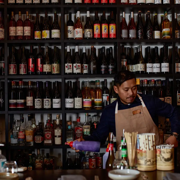 A bartender makes a drink against a backdrop of shelves of wine at Serai Kitchen, one of the best seafood restaurants in Melbourne.